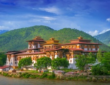 This image captures the serene beauty of Bhutan, showcasing its traditional architecture nestled amidst lush green hills and a calm river flowing by.