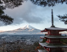 A breathtaking landscape featuring Mount Fuji in the distance and a vibrant red pagoda framed by evergreen trees.