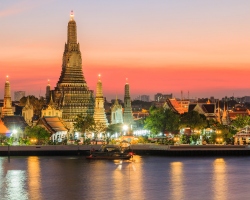 The magnificent Wat Arun Temple glowing in the evening light, with the river reflecting its grandeur under the soft colors of the setting sun.